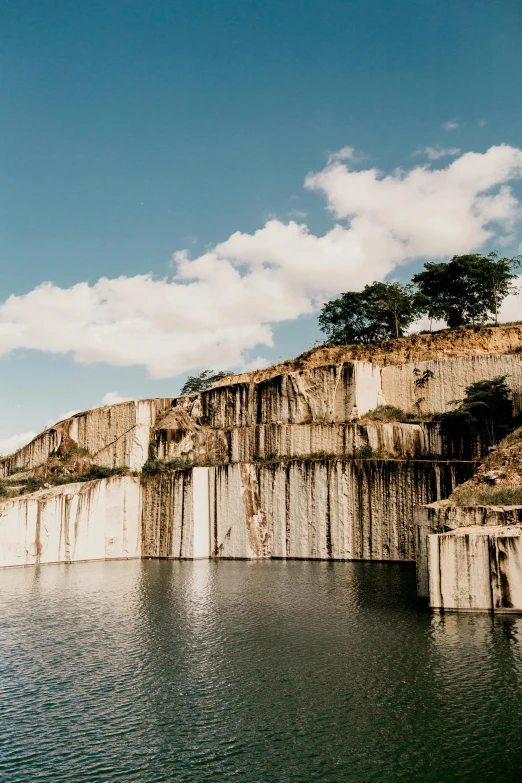 a large body of water next to a cliff, unsplash, brutalism, rock quarry location, marble slabs, puerto rico, water reservoir