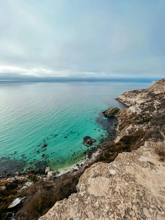 a man standing on top of a cliff next to the ocean, by Terese Nielsen, pexels contest winner, puddles of turquoise water, hollister ranch, 4 k cinematic panoramic view, south african coast