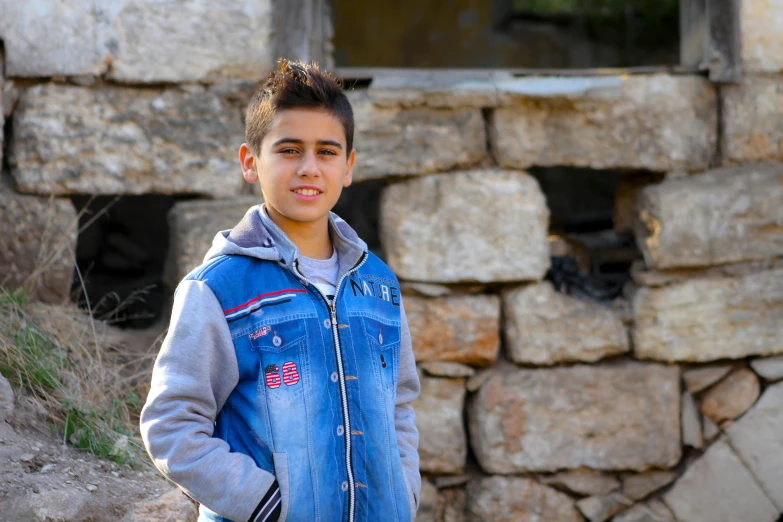 a young boy standing in front of a stone wall, pexels contest winner, les nabis, real life photo of a syrian man, aged 13, 15081959 21121991 01012000 4k, avatar image