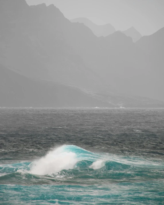 a person windsurfing in the ocean with mountains in the background, a picture, an eerie whirlpool, cyan fog, image