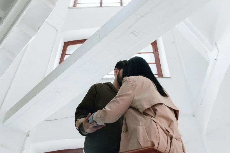 a man and a woman standing next to each other, by Emma Andijewska, pexels contest winner, visual art, inside building, background image, hugging her knees, brown