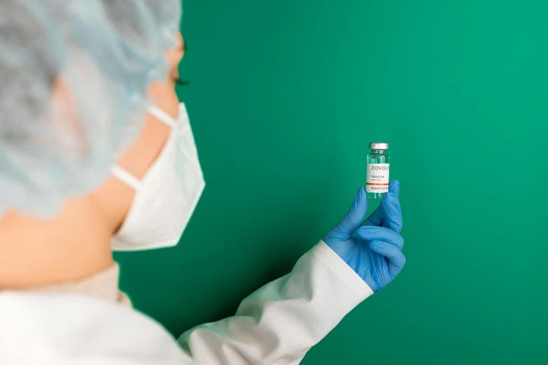 a person in a white lab coat and blue gloves holding a vial, wearing only a green robe, masking, trending photo, petite