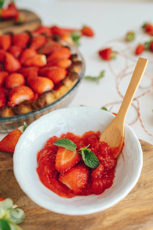 a white plate topped with strawberries next to a pie, wooden bowl, stems, product shot, coral