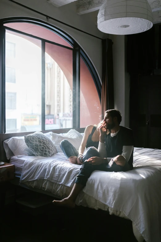 a woman sitting on top of a bed next to a window, couple on bed, hollywood standard, afternoon hangout, brightly lit room