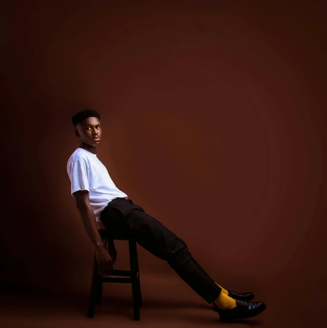 a man sitting on top of a wooden chair, an album cover, unsplash, realism, brown skin, doing an elegant pose, full body photo, on a yellow canva