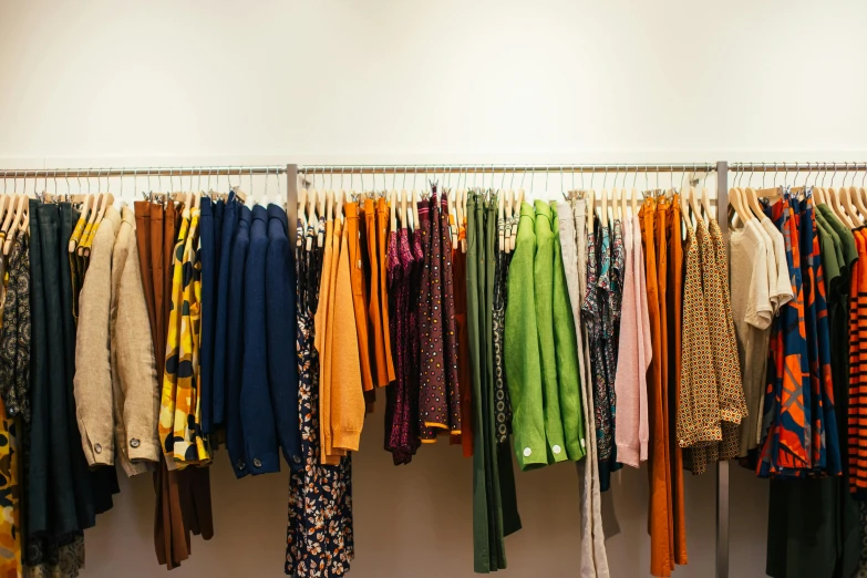 a rack of clothes hanging on a wall, by Nicolette Macnamara, trending on unsplash, 70s colors, diverse costumes, meadows, storefront