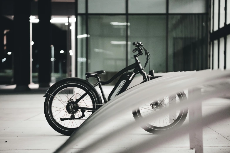 a black and white photo of a bike parked in front of a building, product design shot, eeriewave, warm glow, steel gray body