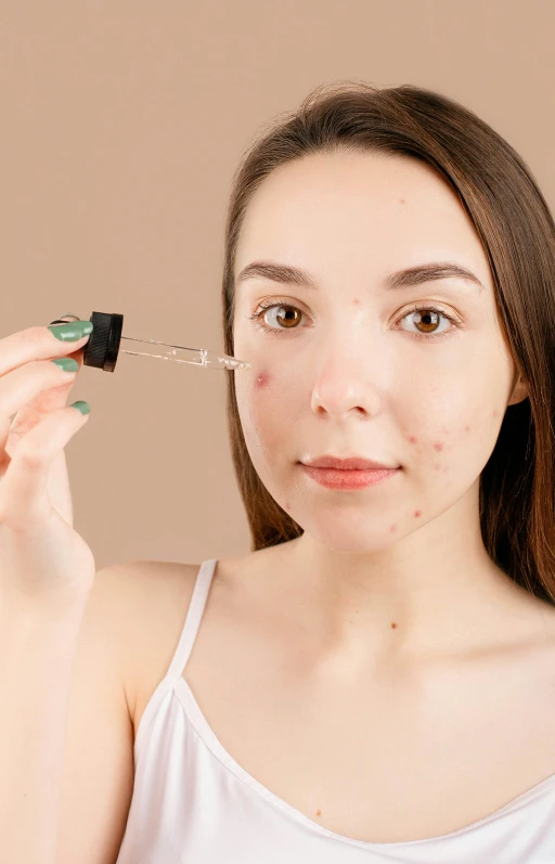 a close up of a person holding a bottle of liquid, by Julia Pishtar, shutterstock, antipodeans, black scars on her face, mole on cheek, 1 9 year old, on a pale background