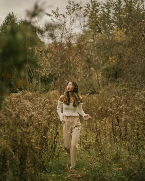 a woman walking through a field of tall grass, trending on pexels, renaissance, brown pants, amongst foliage, portrait sophie mudd, wearing elegant casual clothes