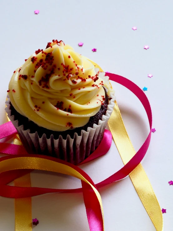 a cupcake with white frosting and red sprinkles, a picture, by Eleanor Best, pexels, ribbon, yellow, maroon, product shot