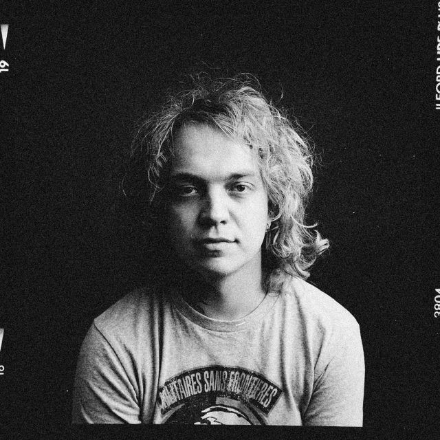a man sitting in front of a laptop computer, a black and white photo, by Lasar Segall, instagram, renaissance, frank dillane, matt mute colour background, blonde man, album cover