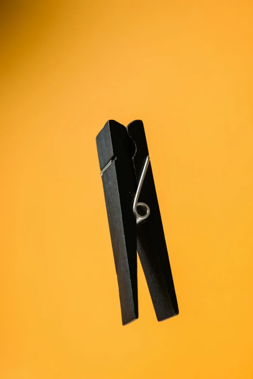 a pair of black clothes pegs on a yellow background, unsplash, portrait n - 9, armature wire, photographed for reuters, dark. no text