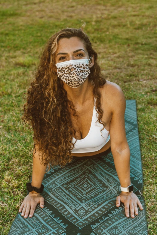 a woman sitting on a yoga mat wearing a face mask, by Carey Morris, in the grass, hispanic, curls, buff