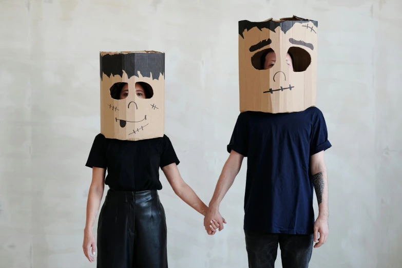 two people standing next to each other with paper bags on their heads, trending on pexels, conceptual art, robot made of a cardboard box, skull mask, etsy, holding hands
