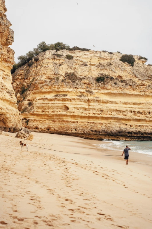 a man walking along a sandy beach next to the ocean, steep cliffs, rocha, chasing a kangaroo, campsites