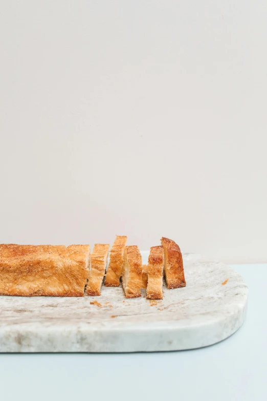 a piece of bread sitting on top of a cutting board, a marble sculpture, by Carey Morris, trending on unsplash, plain background, super long shot, crackles, on a pale background