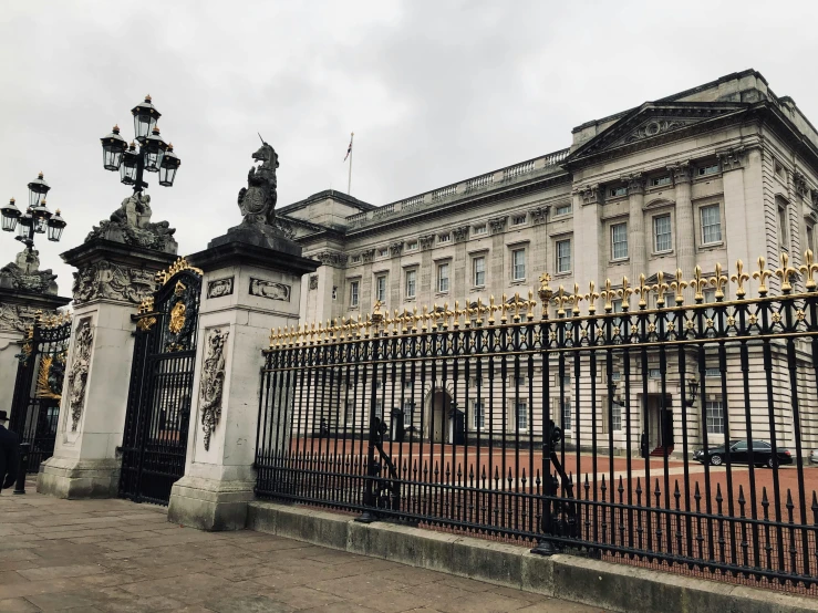 a couple of people that are standing in front of a fence, by Rachel Reckitt, pexels contest winner, baroque, interior of buckingham palace, buildings carved out of stone, thumbnail, 🚿🗝📝