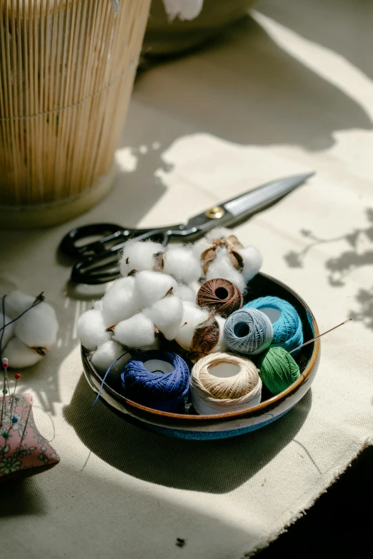 a bowl of yarn and a pair of scissors on a table, a still life, trending on pexels, made of beads and yarn, cotton, gardening, coast