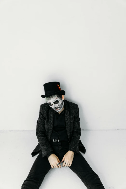 a man in a top hat and suit sitting on a white surface, inspired by James Bolivar Manson, unsplash, conceptual art, skull face paint, full body with costume, lich, album