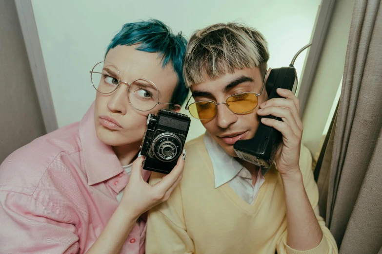 a woman holding a camera next to a man with blue hair, trending on pexels, antipodeans, lesbians, unibrow, cellphone, in retro colors