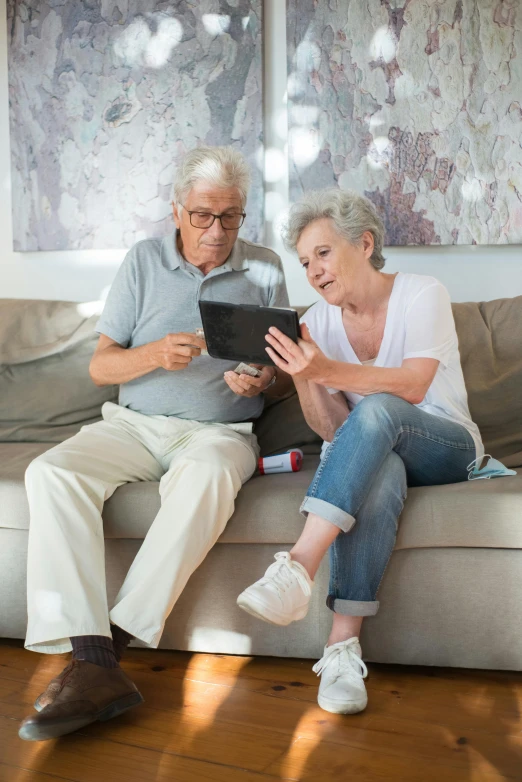 a man and woman sitting on a couch looking at a tablet, elderly, paul barson, multiple stories, a tall