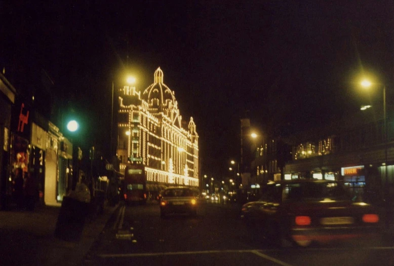 a city street filled with lots of traffic at night, an album cover, by Rupert Shephard, flickr, victorian architecture, 35mm film still from 1994, christmas lights, medium format. soft light