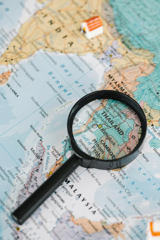 a magnifying glass sitting on top of a map, south east asian with round face, detailed product image, zoom shot, large shot