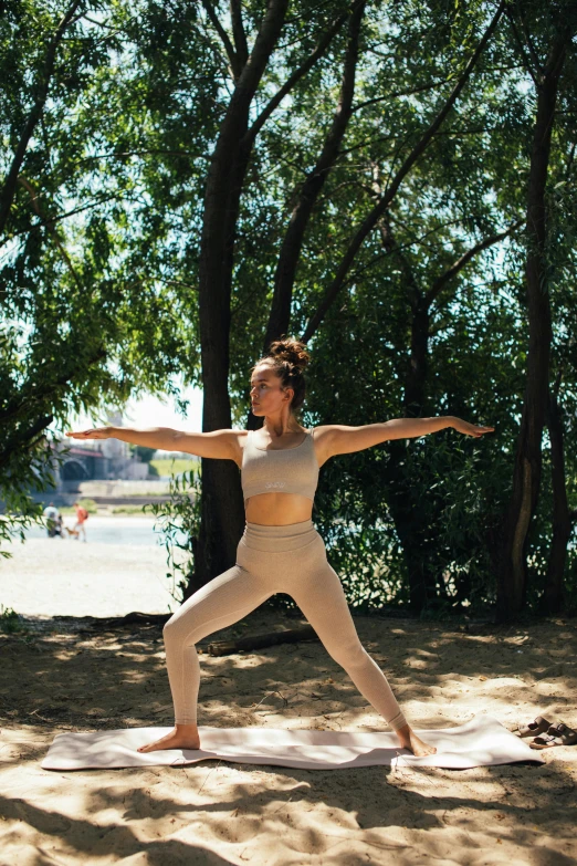 a woman doing a yoga pose in the sand, by Carey Morris, unsplash, arabesque, in a city park, against the backdrop of trees, slightly sunny, back arched