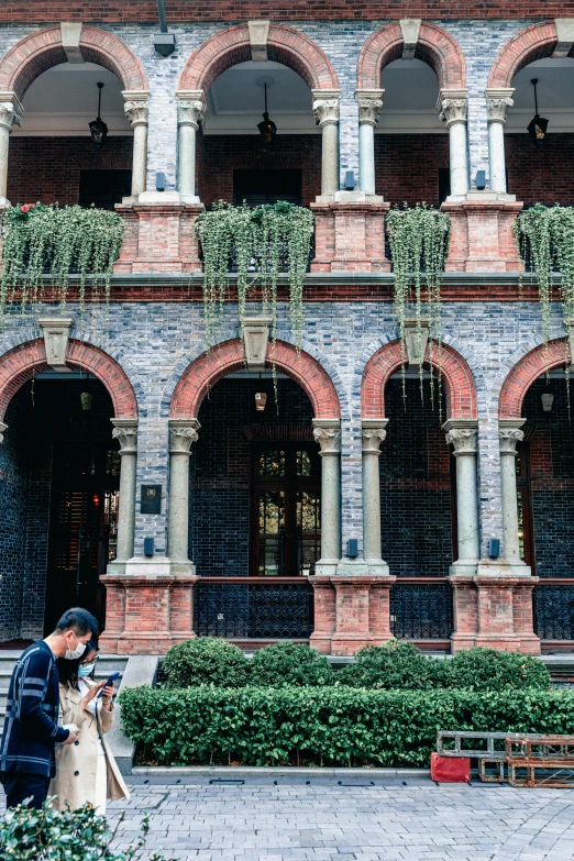 a couple of people that are standing in front of a building, inspired by Sydney Prior Hall, pexels contest winner, heidelberg school, archways made of lush greenery, shanghai, cai xukun, brick building