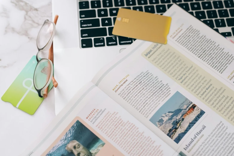 a laptop computer sitting on top of a desk, by Julia Pishtar, trending on unsplash, clippings of a fashion magazine, tourism, open books, pair of keycards on table