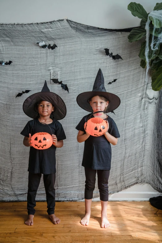 two children in halloween costumes holding pumpkins, by Nina Hamnett, pexels contest winner, vantablack wall, black pointed hat, photo booth, no - text no - logo