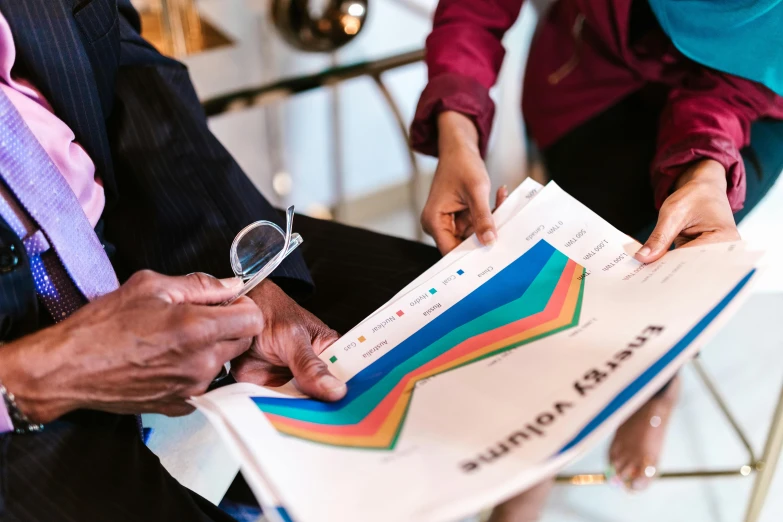 a close up of a person holding a magnifying glass, graphs, multicoloured, thumbnail, papers on table