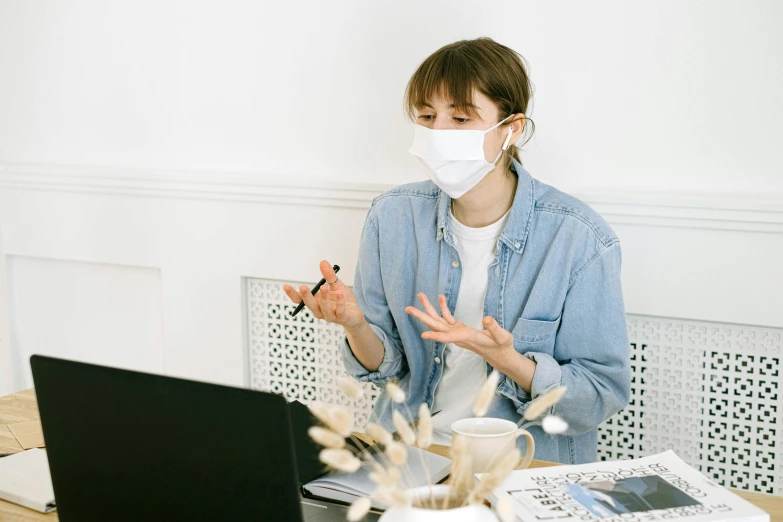 a woman sitting at a table with a laptop and wearing a face mask, a picture, demo scene, clean aesthetic, busy room, thumbnail