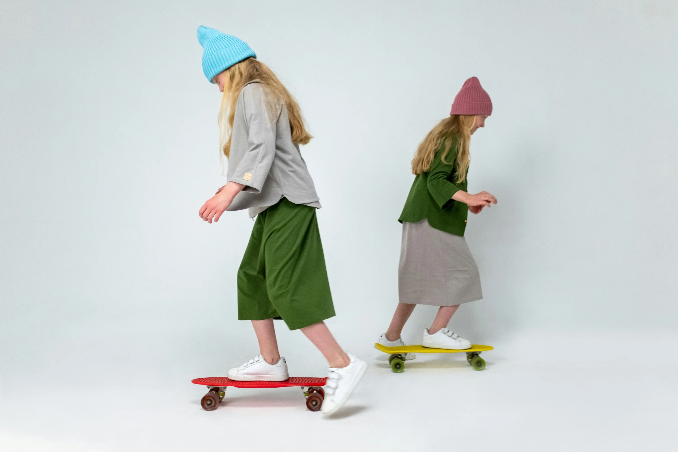 a couple of kids riding skateboards on a white surface, inspired by Elsa Beskow, trending on pexels, knitted hat, olive green and venetian red, nun fashion model, natural wood top
