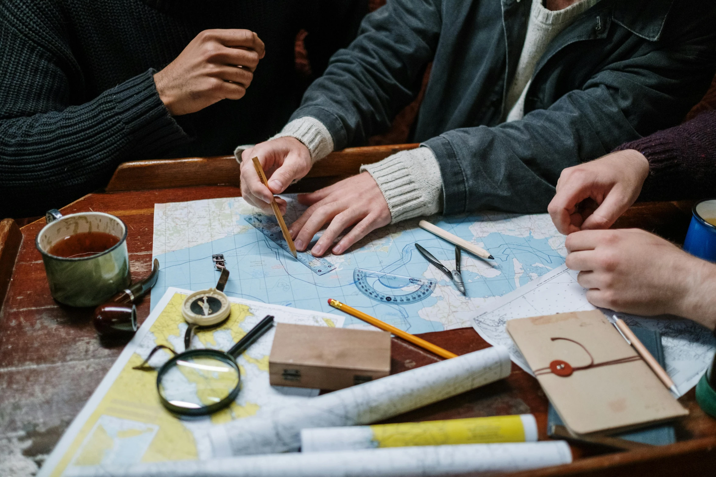 a group of people sitting around a wooden table, nautical maps, adventure, knolling, canva