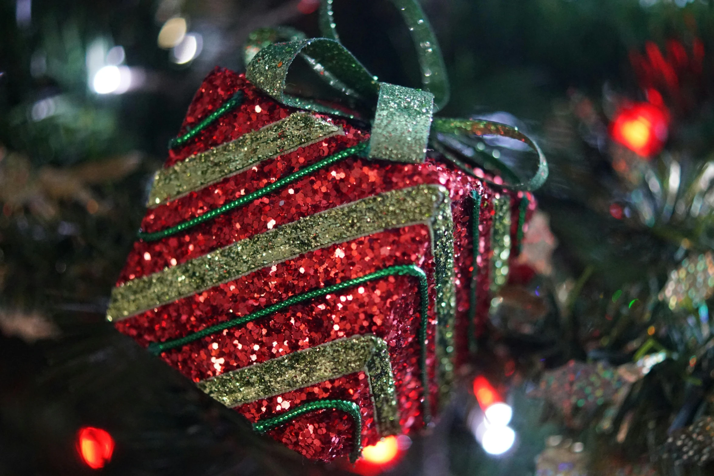 a christmas ornament hanging from a christmas tree, by Alice Mason, pexels, red and green color scheme, square, glitter gif, wrapped