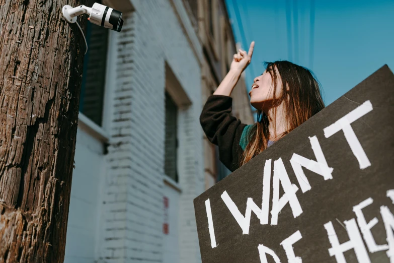 a woman holding a sign that says i want health, trending on pexels, graffiti, security camera photo, raised hand, future activist, teenage girl