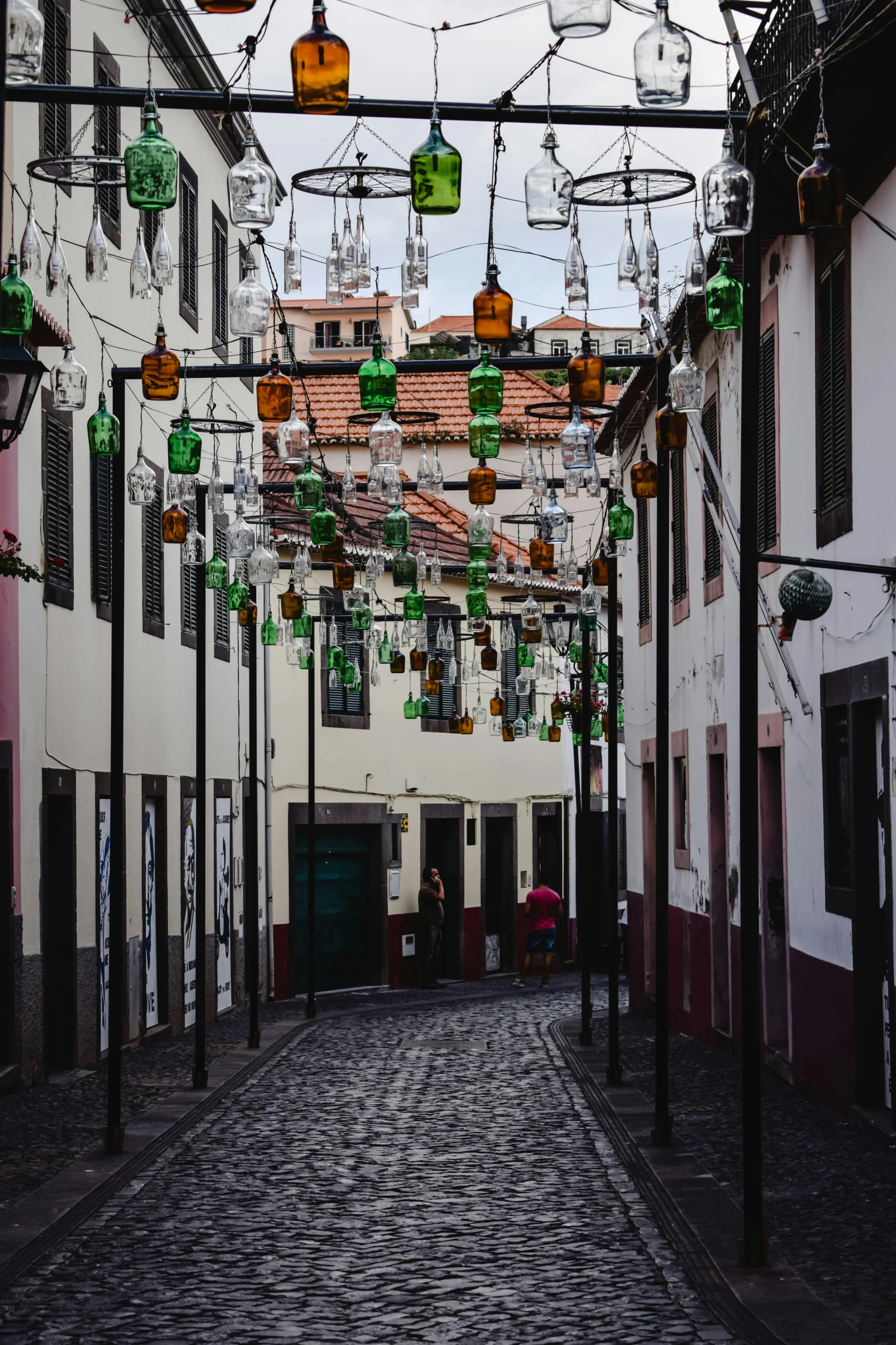 a narrow cobblestone street with a clock tower in the background, pexels contest winner, graffiti, hanging tiffany chandeliers, azores, beer bottles, red and green color scheme