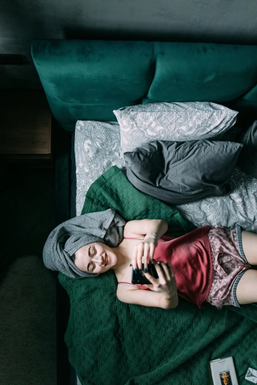 a person laying on a bed with a cell phone, a portrait, inspired by Elsa Bleda, renaissance, lush green, grey, high angle, ignant