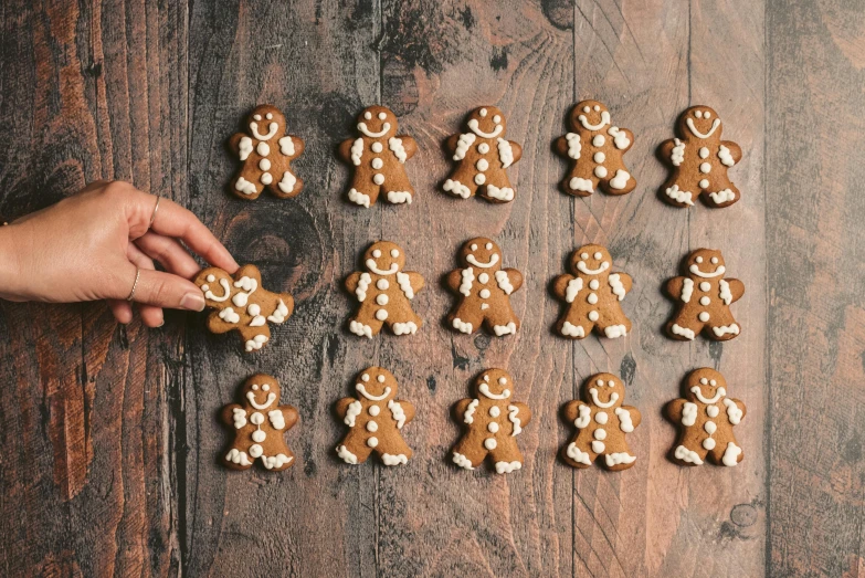 a person reaching for gingerbreads on a wooden table, by Emma Andijewska, pexels, folk art, 🎨🖌️, in a row, cutest, clones