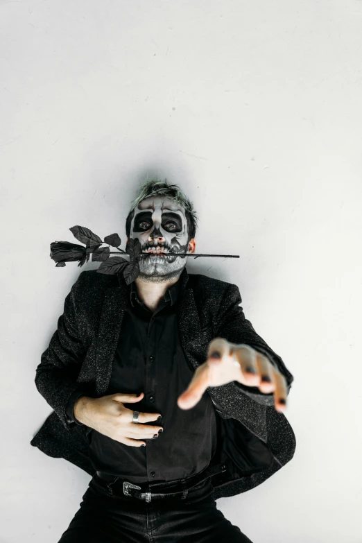 a man dressed as a skeleton with a knife in his mouth, an album cover, inspired by Nicola Samori, reddit, on a gray background, ( ( ( el dia los muertos ) ) ), shot from above, disney and dan hillier