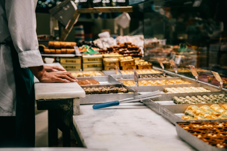 a man standing in front of a counter filled with lots of food, trending on pexels, process art, pastry, melbourne, inspect in inventory image, all marble
