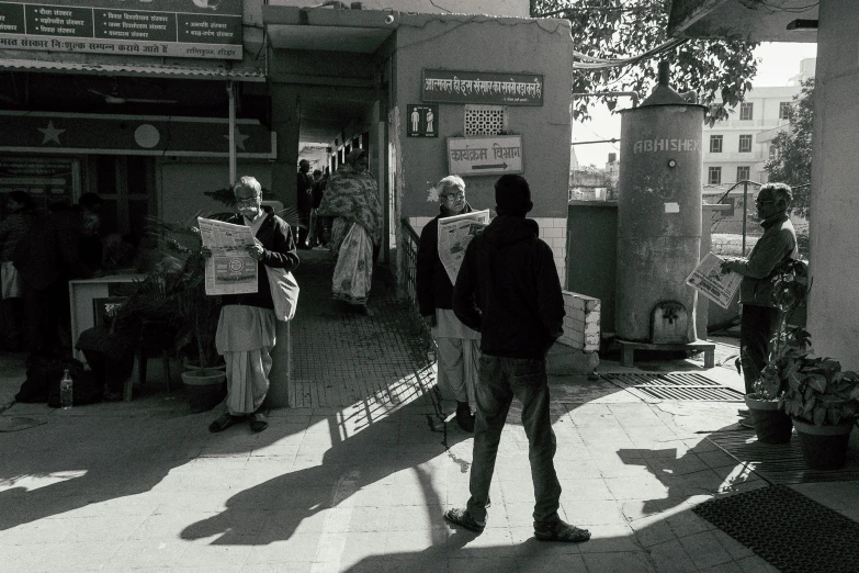 a group of people standing next to each other on a sidewalk, by Narayan Shridhar Bendre, private press, reading the newspaper, high shadow, instagram photo, exiting store