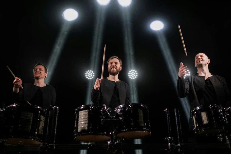 a group of men standing next to each other holding drums, an album cover, by Julia Pishtar, unsplash, light show, hyper realistic, the three moiras, dark. no text