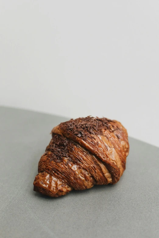 a croissant sitting on top of a table, chocolate. rugged, brown resin, with a soft, spike shell