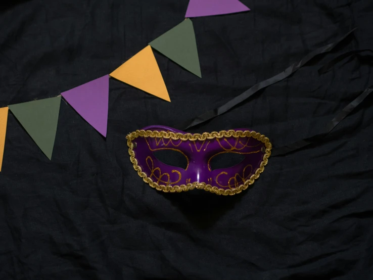 a purple mask sitting on top of a black table, inspired by Mardi Barrie, pexels contest winner, renaissance, cloth banners, yellow purple green, flatlay, party