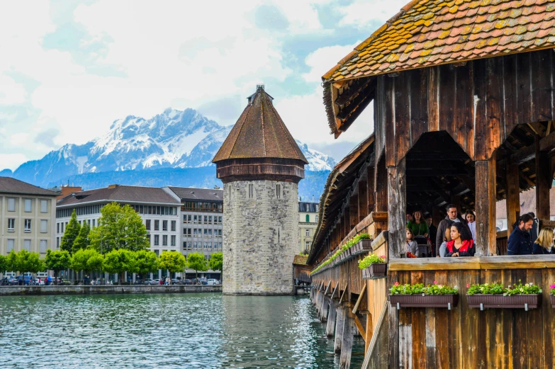 a group of people standing on a pier next to a body of water, a cartoon, pexels contest winner, renaissance, alpine architecture, portcullis, swiss alps, all buildings on bridge