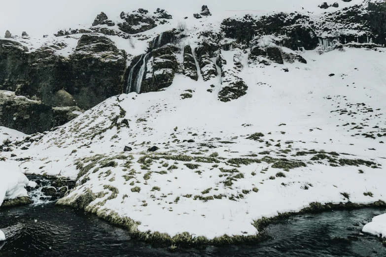 a man standing on top of a snow covered mountain, by Hallsteinn Sigurðsson, pexels contest winner, hurufiyya, waterfall falling into a lake, thumbnail, subtle details, ground covered with snow