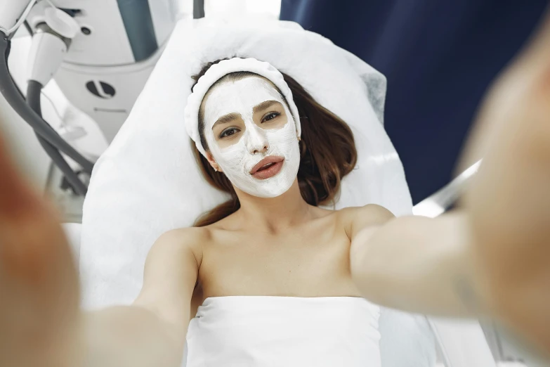 a woman getting a facial mask at a beauty salon, by Julia Pishtar, happening, accidentally taking a selfie, wearing white silk hood, square facial structure, 8k quality
