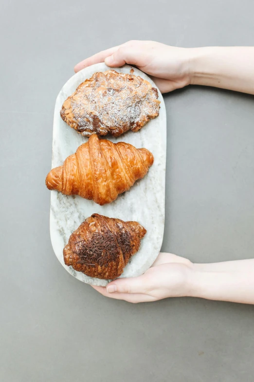 a person holding a plate with croissants on it, inspired by Richmond Barthé, granite, resin, bakery, white
